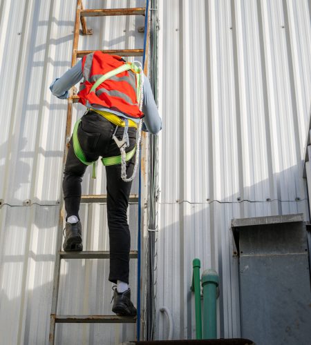 Construction worker wearing safety harness belt during working on roof structure of building on construction site.
